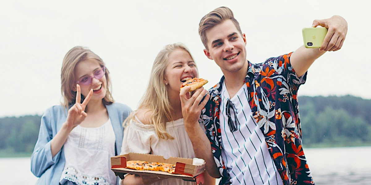 3 personer spiser pizza og tar selfie